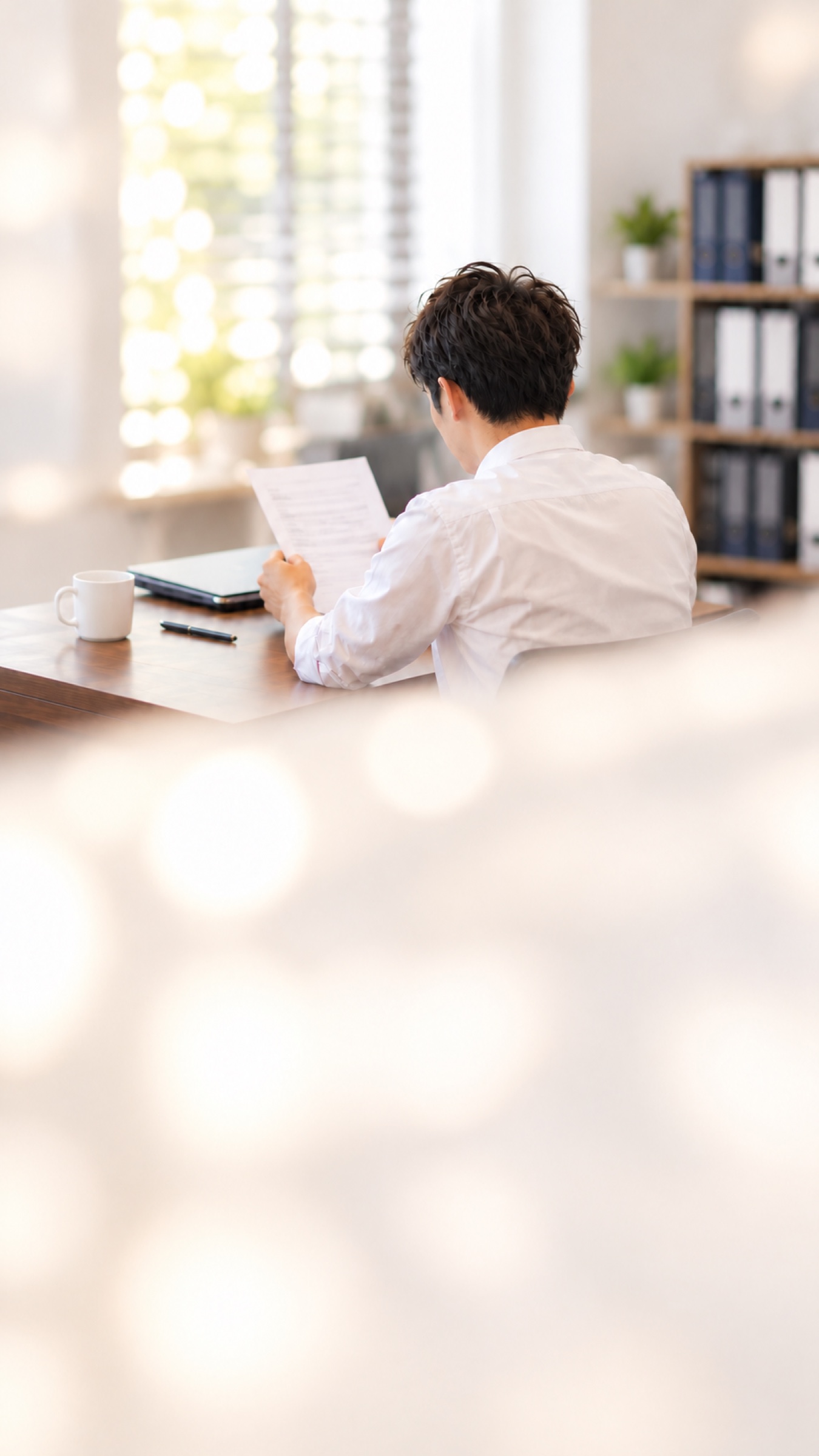 窓辺の机で書類に目を通す男性